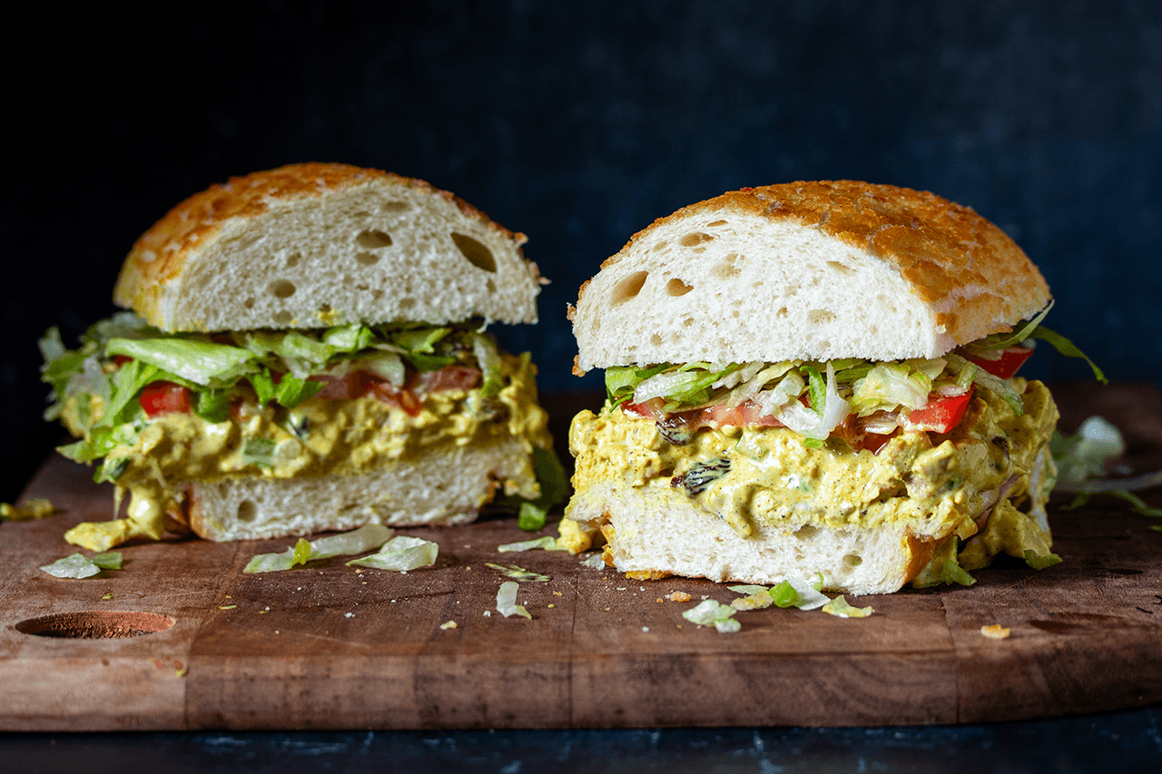 A chicken salad sandwich cut in half and both halves sitting on a wooden board.