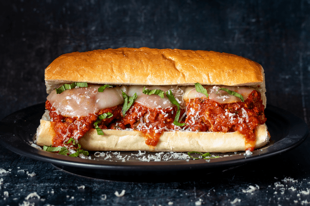 Front long view of a meatball sub on a black plate.
